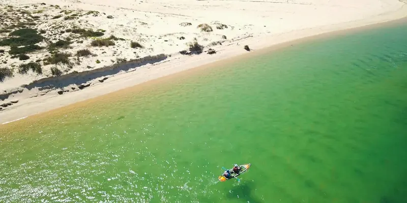 A kayak paddles along a white sandbank beach with dunes
