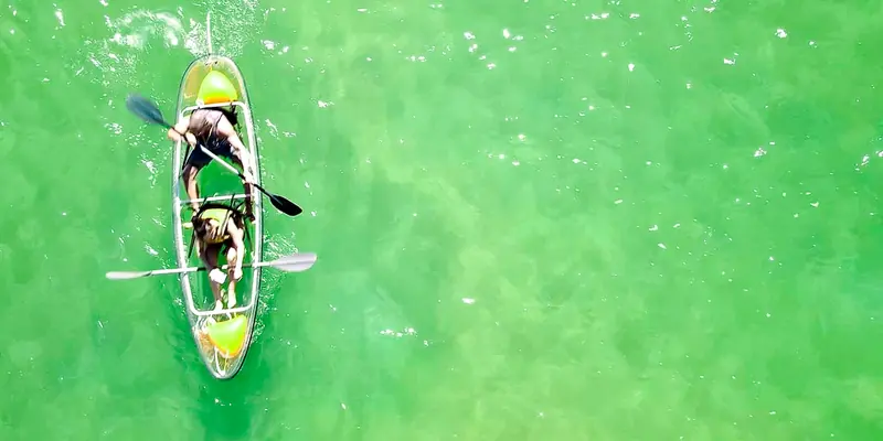 A clear kayak on bright green water seen from a drone