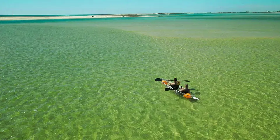 A clear kayak crosses turquoise shallows near a sandbank