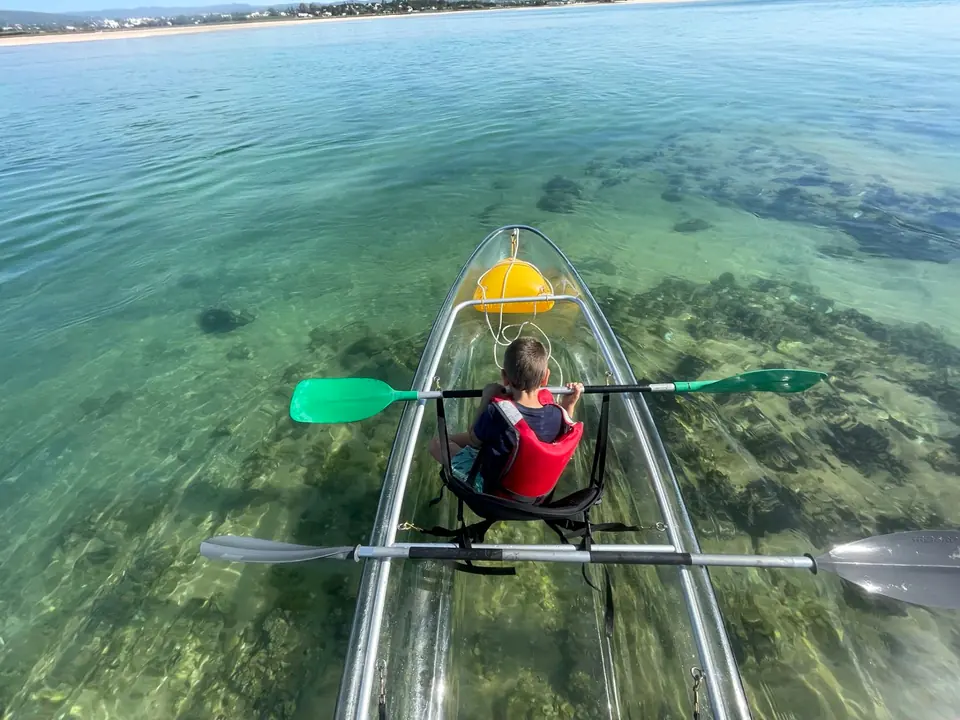 A child paddles a transparent kayak over seagrass in the Ria Formosa lagoon