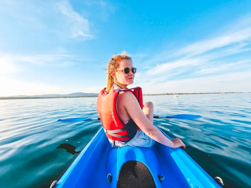 A paddler in a blue sit-on-top kayak on calm lagoon water